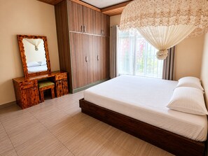 Een slaapkamer met een houten garderobe, een nachtkastje met lades, een groot bed met wit beddengoed en een raam met gordijnen.