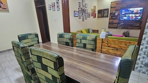 A dining area with a wooden table and patterned chairs, a green sofa, and a TV mounted on the wall. - Secure 4BR Home Near City Center (Kigali)