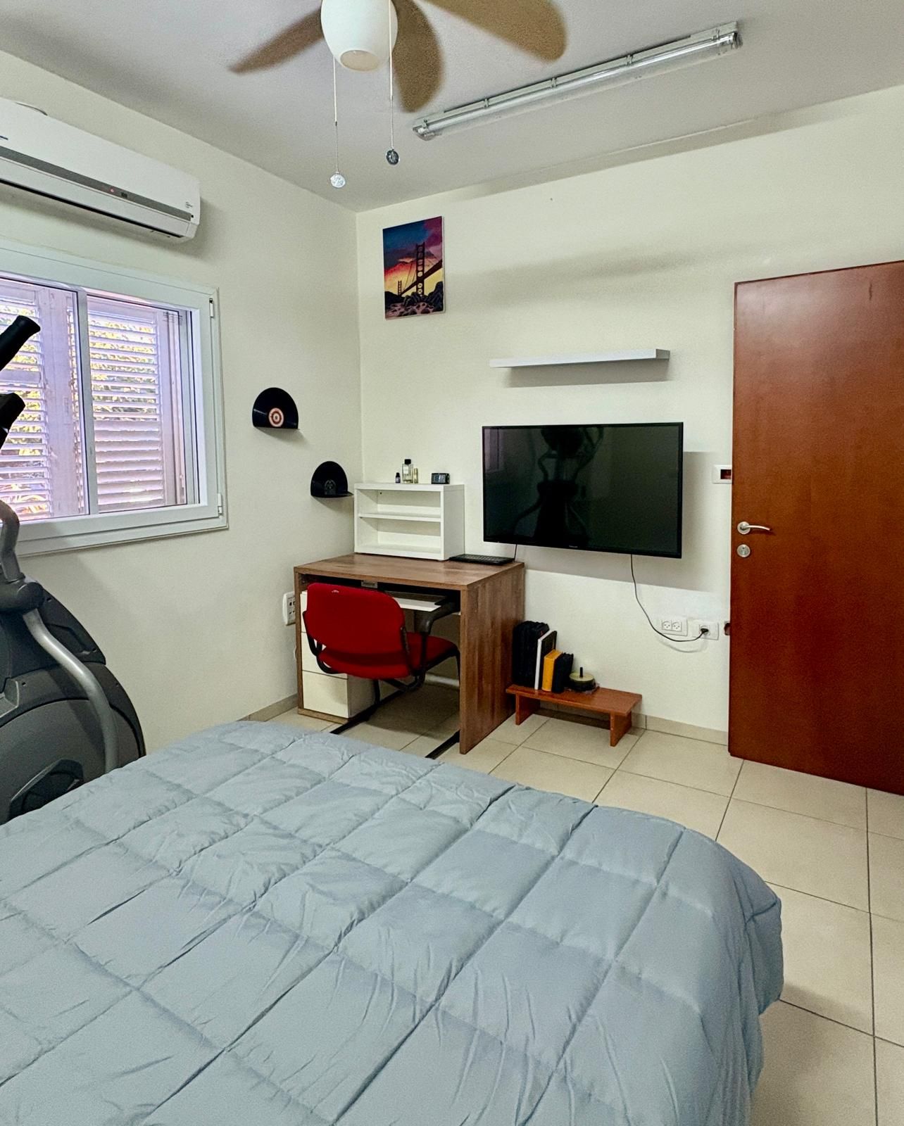 A bedroom with a bed, a desk, a chair, a television, and a wardrobe.
