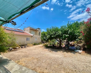 A residential property with a gravel driveway, a house with a red-tiled roof, and a garden with trees and shrubs.