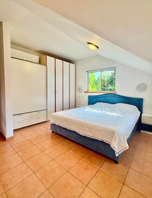 Quarto com cama, guarda-roupa, janela com vista para vegetação e luminária no teto.