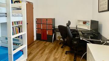 Een kamer met een houten vloer, een bureau met een computer, een stoel, een boekenkast en een plafondventilator.