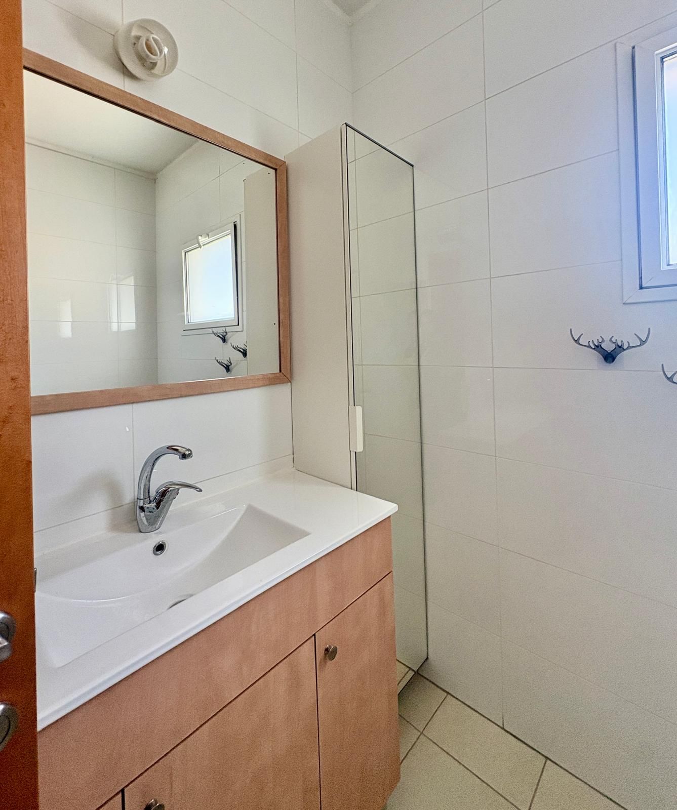 Ein Badezimmer mit einem weißen Waschbecken, einem Spiegel und einer Duschkabine aus Glas.
