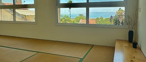Una habitación con tatamis, amplias ventanas con vista al mar y una mesa de madera con un jarrón.
