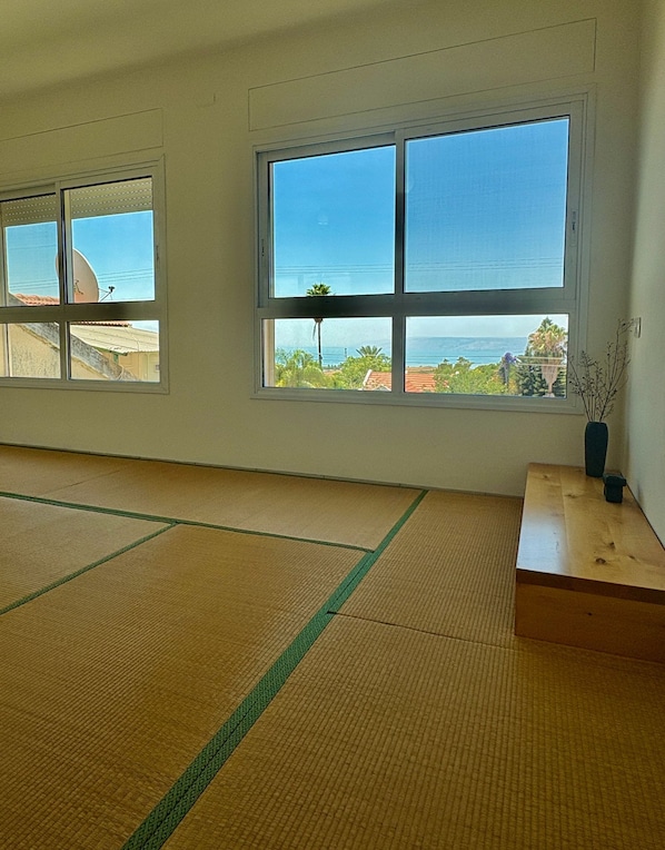 A room with tatami mats, large windows with a view of the sea, and a wooden table with a vase.