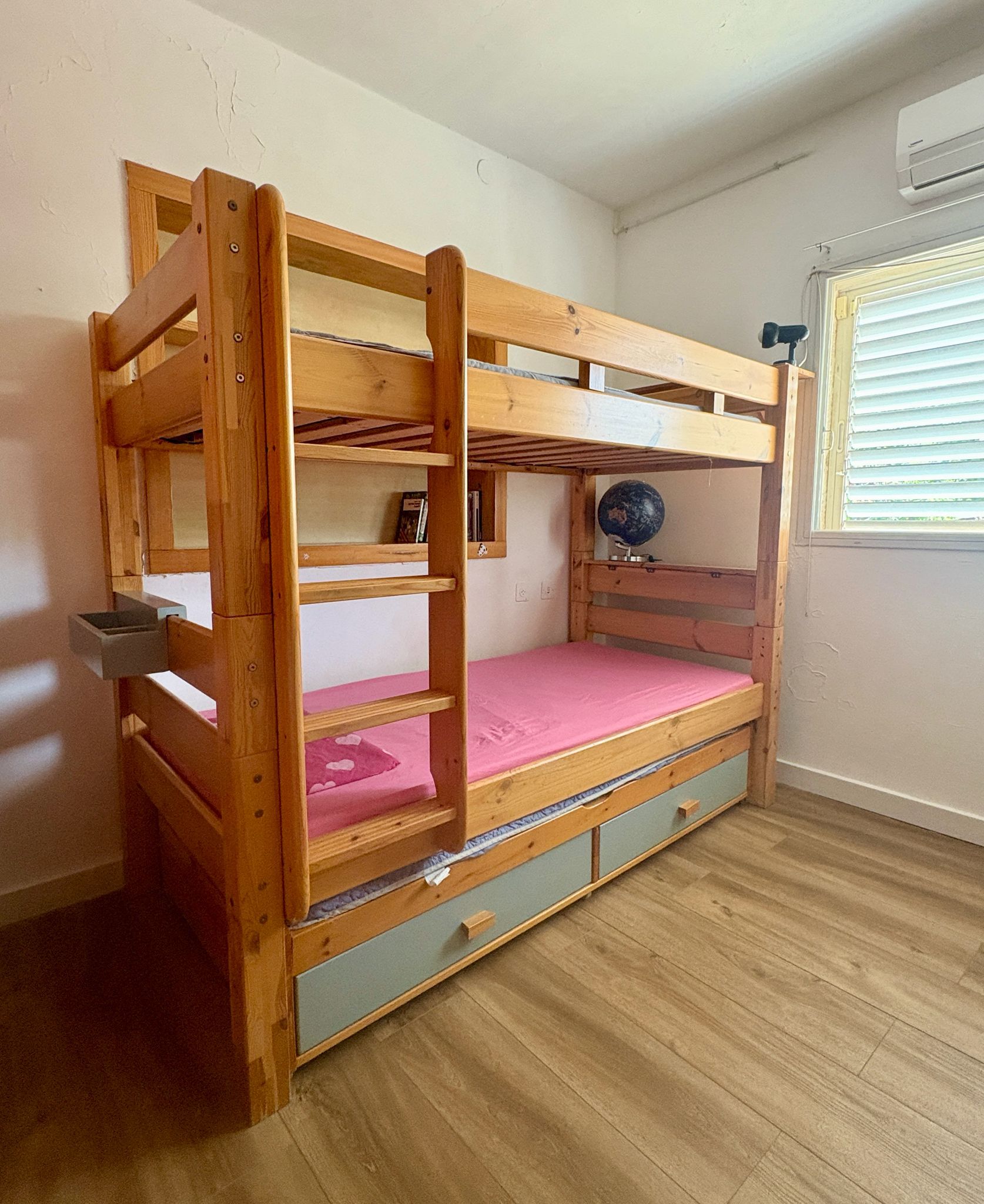 Ein Etagenbett mit ausklappbarem Schreibtisch und Schubladen, ein Globus auf dem oberen Bett und ein Fenster mit Jalousien.