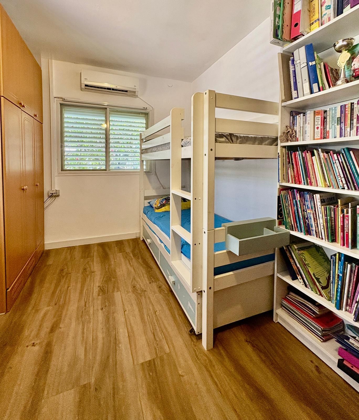 A room with a bunk bed, a bookshelf, and an air conditioning unit.