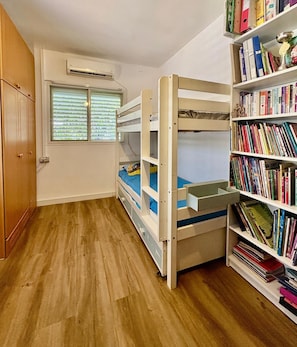 Een kamer met een stapelbed, een boekenkast en een airconditioning.