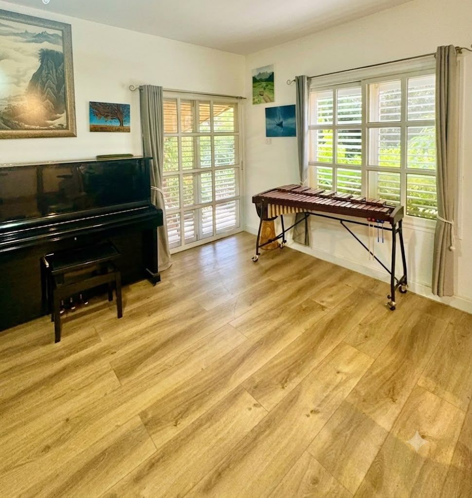 Ein Zimmer mit Klavier, Fernseher und einem fensterbepflanzten Fenster.