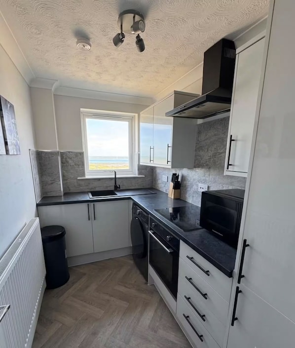 A compact kitchen with a window, built-in oven, and a black countertop.