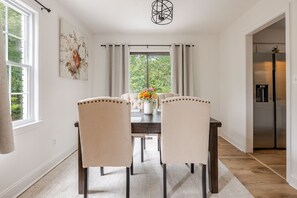 Un espace repas comprenant une table, des chaises, un lustre et une vue sur la verdure environnante.