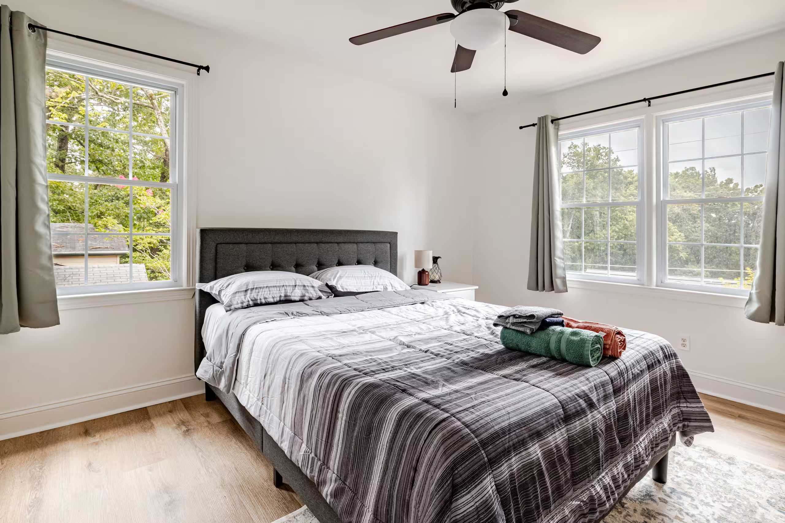 Un dormitorio con cama, ventilador de techo y ventanas amplias.
