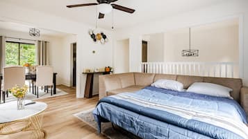 Un dormitorio con cama, ventilador de techo, una mesa con un jarrón y vistas al exterior.