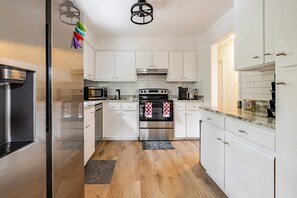 A modern kitchen with white cabinets, stainless steel appliances, and a marble countertop.