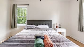 Een slaapkamer met een groot bed, een nachtkastje, een raam met gordijnen en uitzicht op bomen.