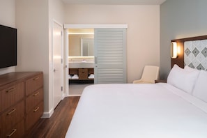 Een hotelkamer met een groot bed, een houten dressoir, een televisie, een badkamer met een spiegel en een inloopkast.