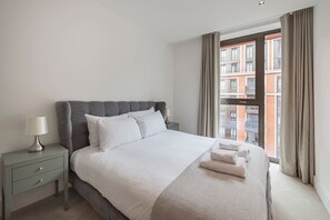 Een hotelkamer met een bed, een nachtkastje, een lamp en uitzicht op een gebouw door het raam.