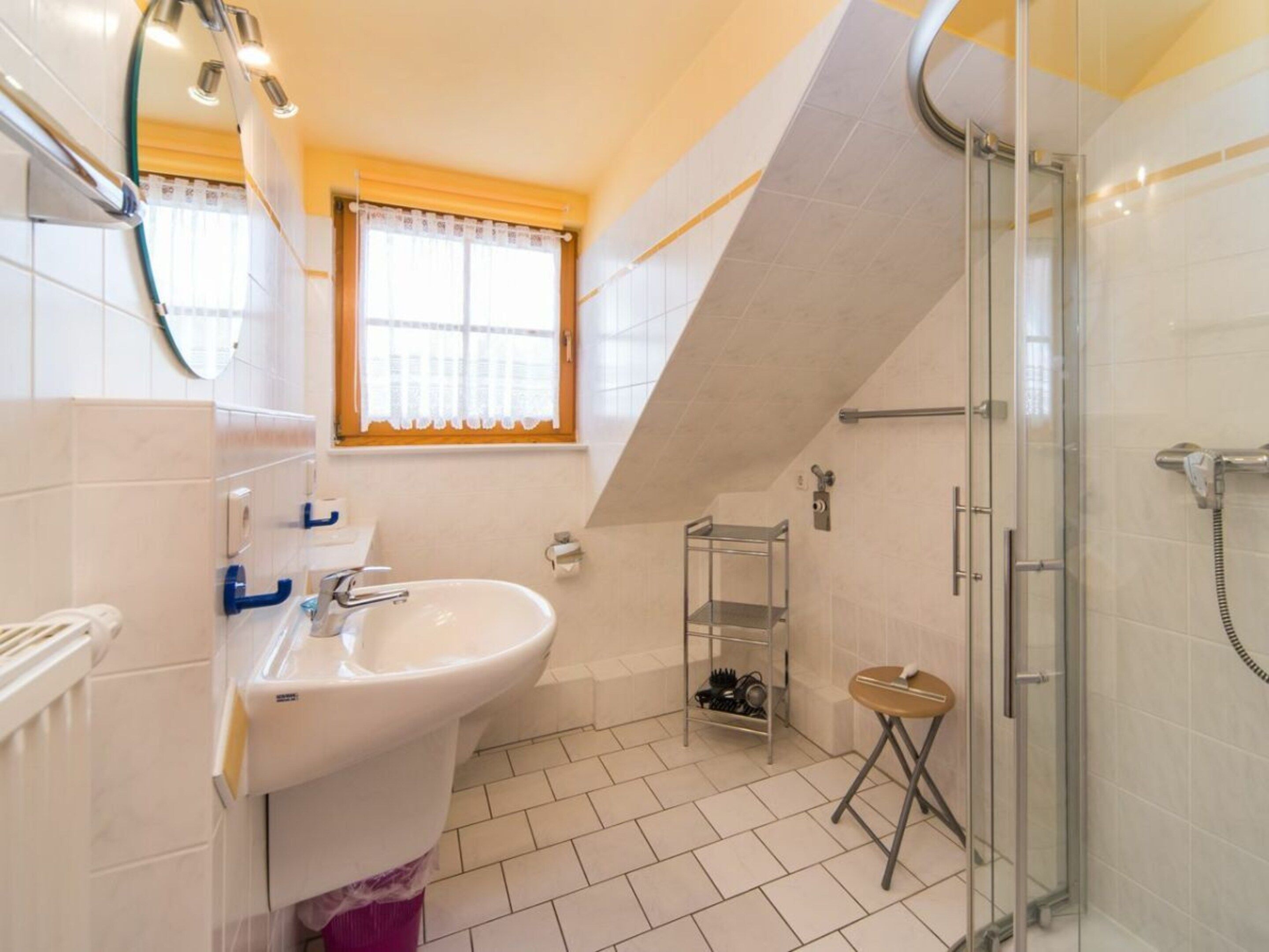 Een badkamer met een wastafel, spiegel, douche en een raam met gordijn.