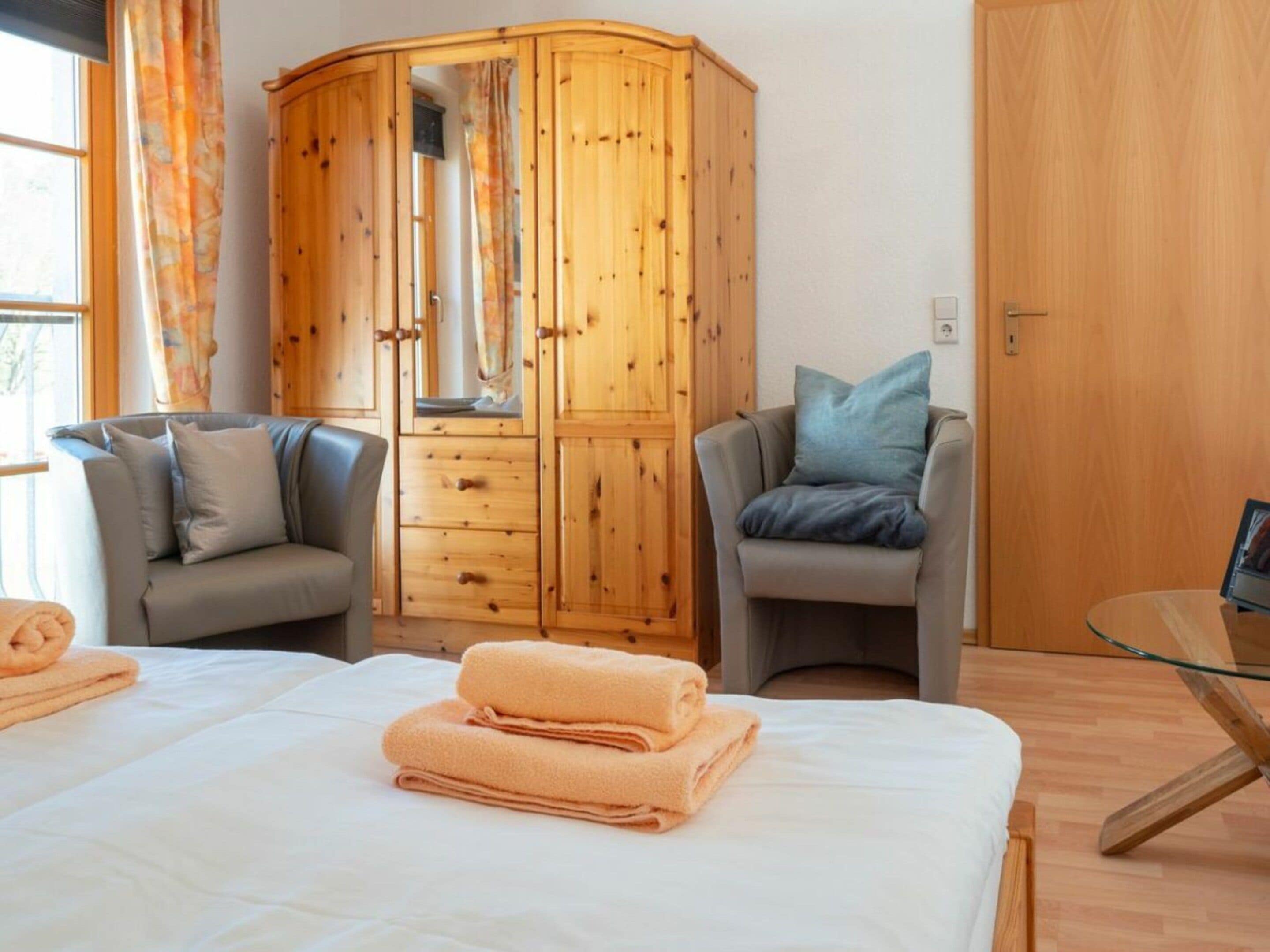 Een slaapkamer met een bed, twee fauteuils, een houten garderobe en een glazen tafel.