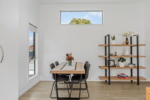 A modern dining area with a wooden table, black chairs, and a bookshelf with plants and books. - Invermay Escape Stay Close to Stadium and Museums (Invermay)