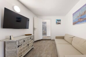 A modern living room with a flat-screen TV, a wooden cabinet, a beige sofa, and a door leading to another room. - Home2Book Casa Yoyo Lanzarote Coastal Home (El Golfo)