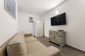 A living room with a beige sofa, a white cabinet, a flat-screen TV mounted on the wall, and a painting on the wall. - Home2Book Casa Yoyo Lanzarote Coastal Home (El Golfo)