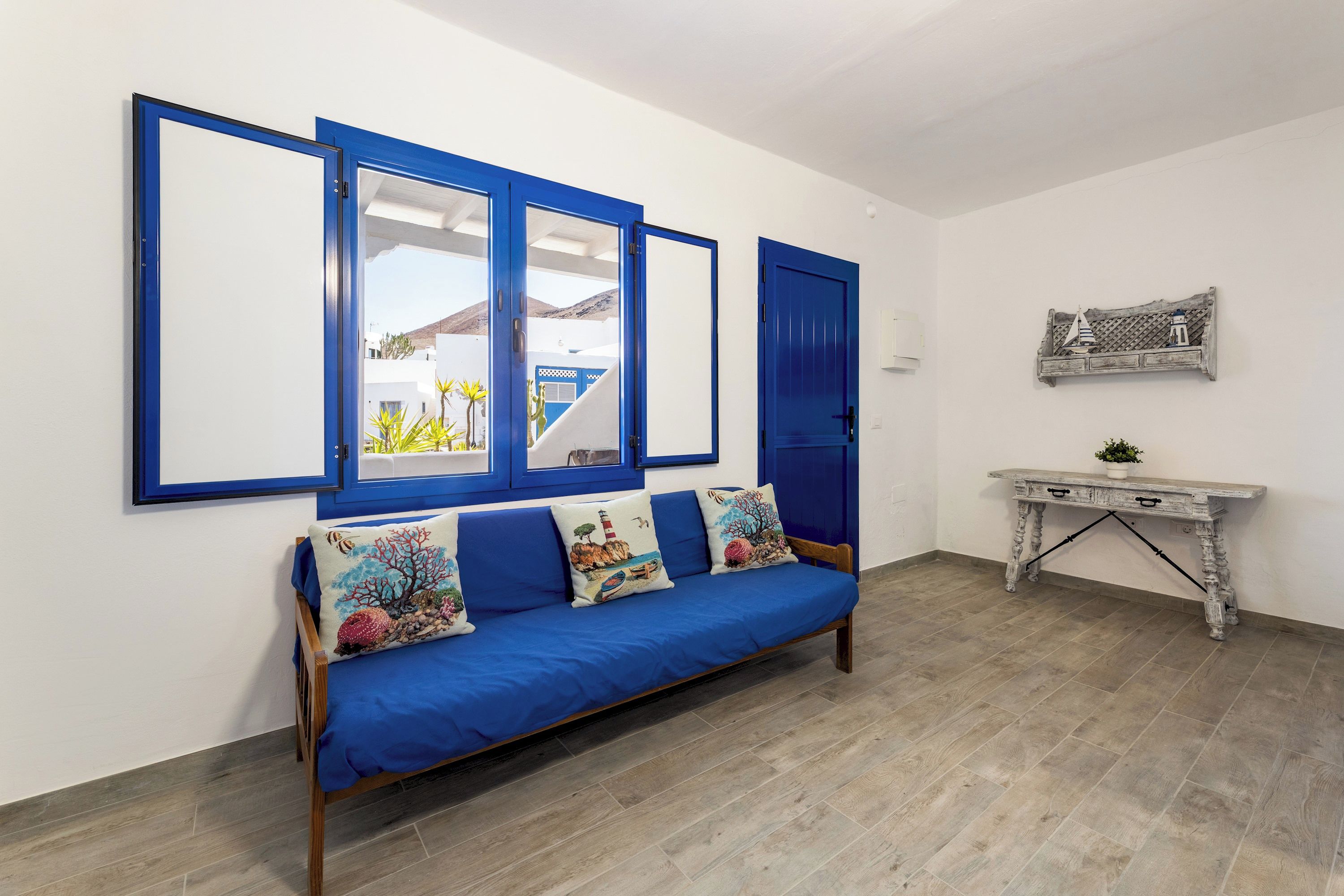 A room with a blue sofa, a white console table, and a wall-mounted shelf with decorative items.