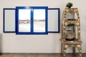 A room with a blue-framed window overlooking a barren landscape, a decorative shelf with seashells, and a small potted plant. - Home2Book Casa Yoyo Lanzarote Coastal Home (El Golfo)