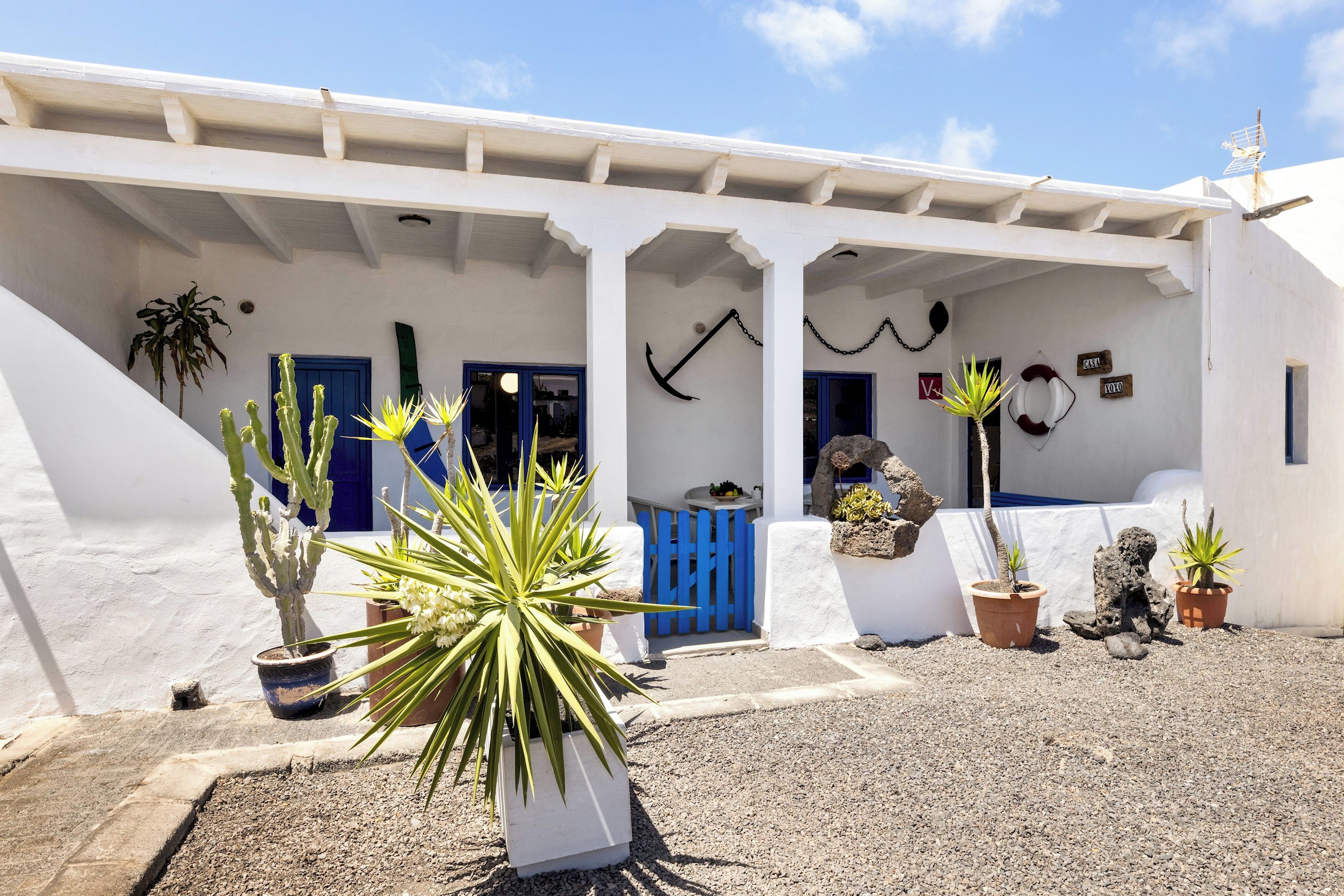A white building with a covered entrance, potted plants, and a blue door.