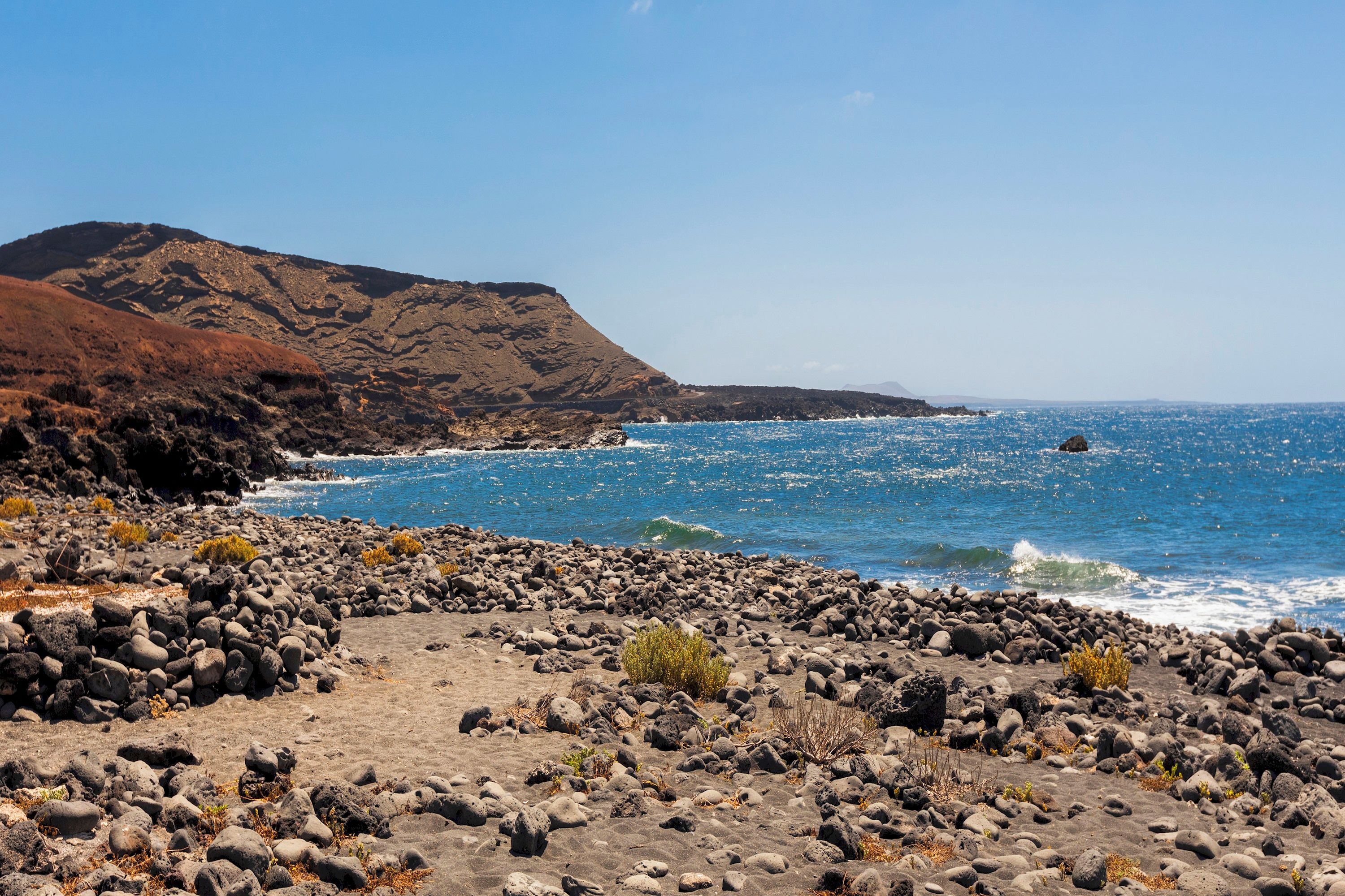 A rocky coastline with a clear view of the ocean and a mountain in the background.
