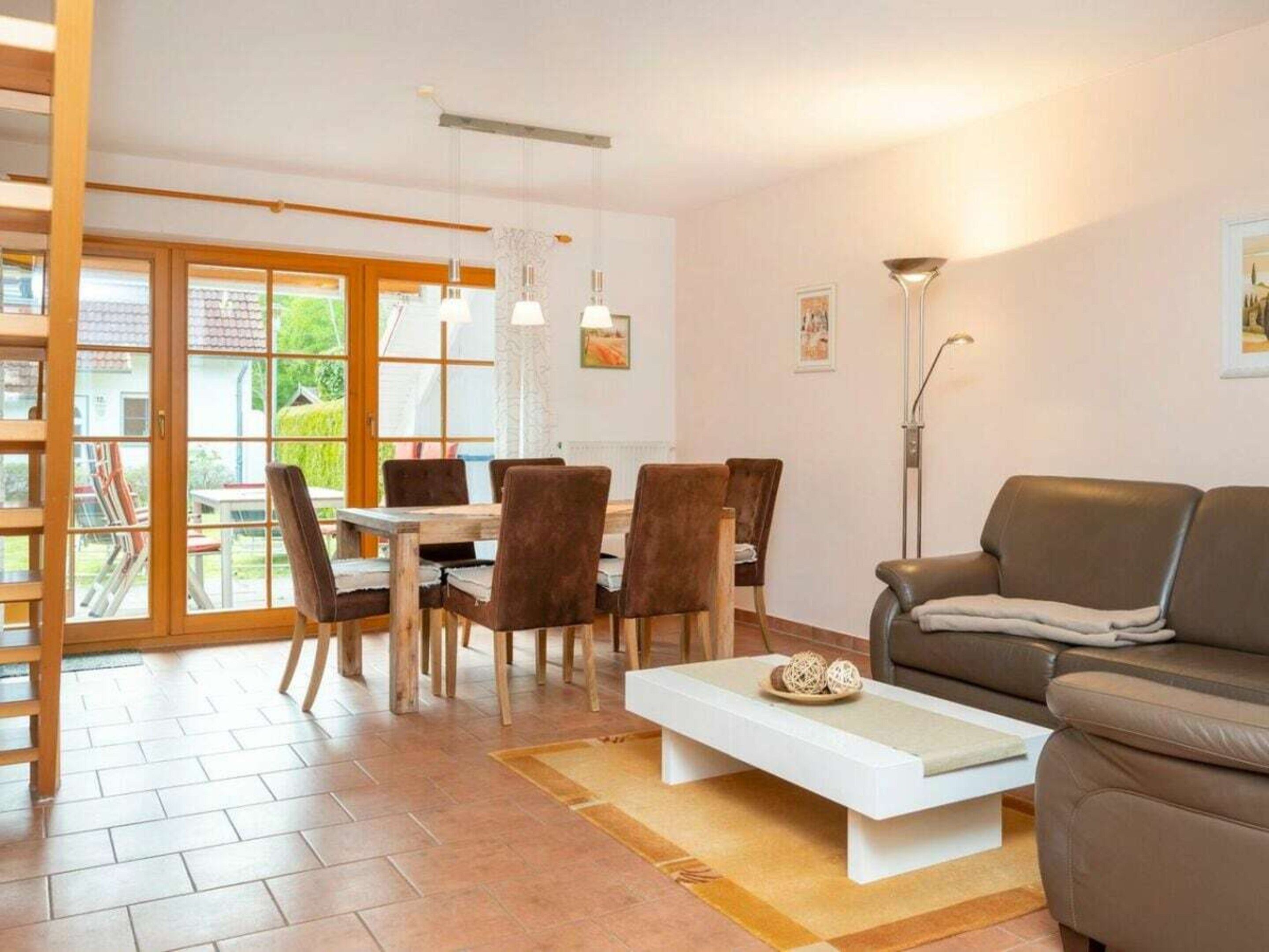 A modern living room with a sofa, a dining table with chairs, and a large window with a view of the outdoors.