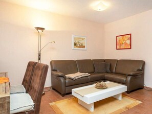 A living room with a brown leather sofa, a white coffee table, a floor lamp, and two framed pictures on the wall. - 8b/t5 Holiday Home Park \"freesenbruch\" (Zingst)