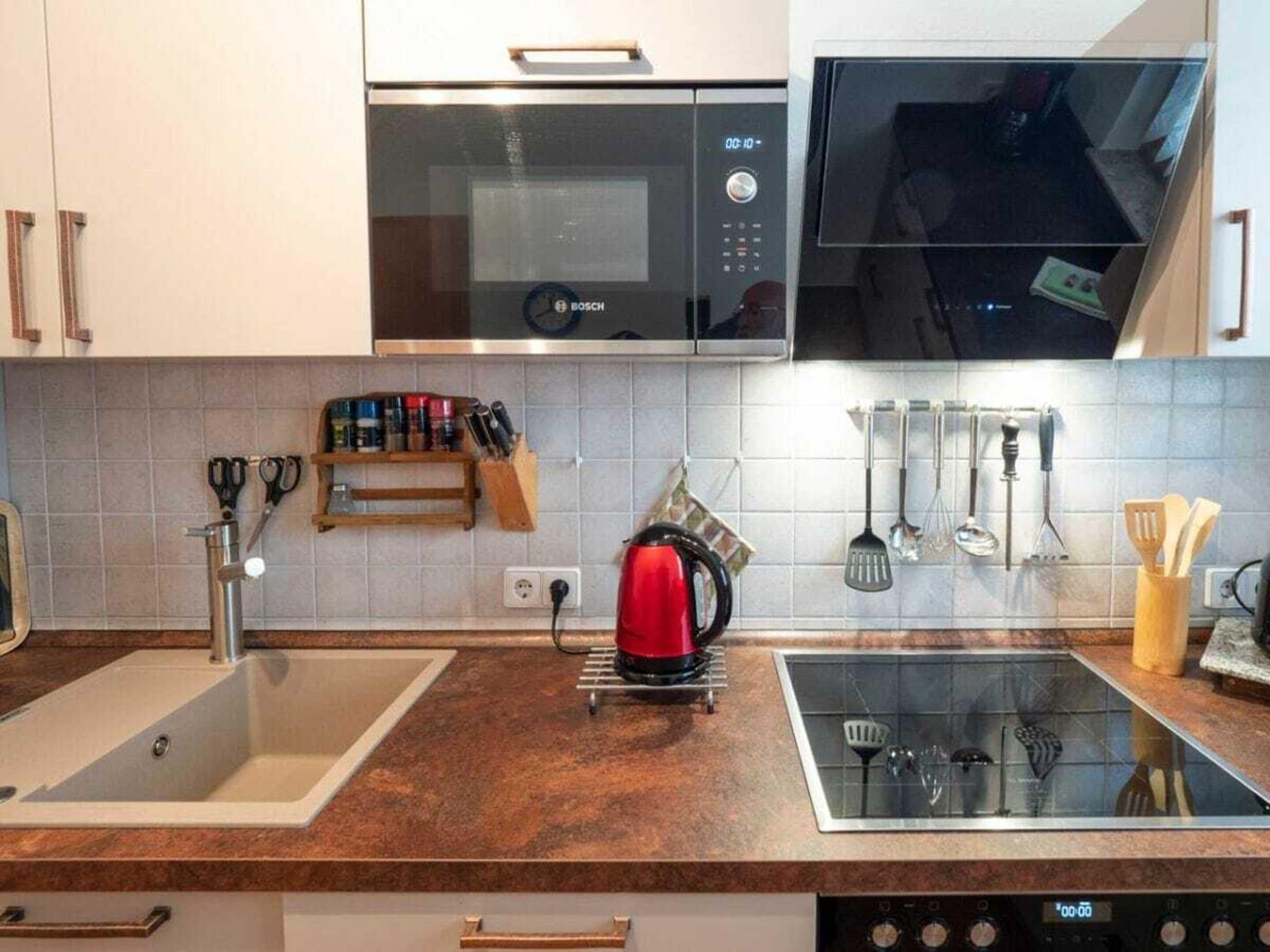 A kitchen with a Bosch microwave, a red kettle, and a glass stovetop.