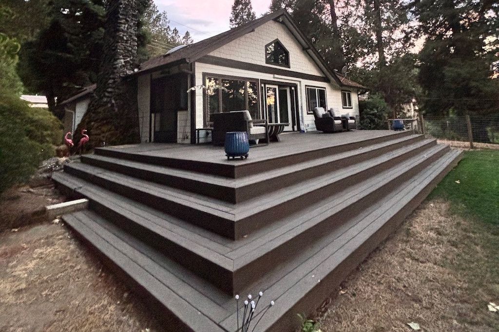 A house with a wooden deck, a covered porch, and a stone wall.