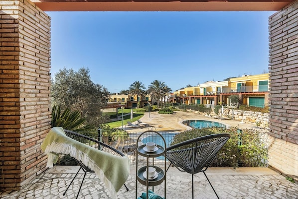 Ein Balkon mit Blick auf einen Swimmingpool, Liegestühlen und eine Backsteinmauer.