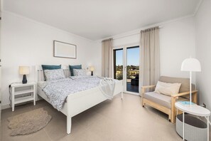 Ein Schlafzimmer mit einem Bett, Nachttischen, einem Sessel, einem kleinen Tisch und Blick durch eine Schiebetür.