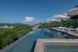 A modern infinity pool with a clear view of the ocean and mountains, surrounded by lounge chairs and umbrellas. - Casa Mare Luxury Estates Rentals At Kupuri (Punta Mita)