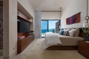 A modern bedroom with a large bed, a flat-screen TV, a view of the sea, and a colorful abstract painting. - Casa Mare Luxury Estates Rentals At Kupuri (Punta Mita)