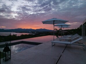 A poolside area with lounge chairs and umbrellas, overlooking a body of water and mountains. - Casa Mare Luxury Estates Rentals At Kupuri (Punta Mita)