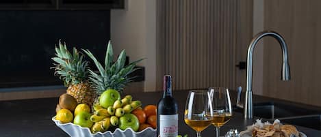 Una isla de cocina con un cuenco de frutas, una botella de vino, vasos y una cesta de pan.
