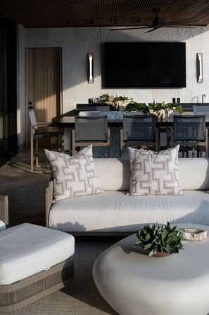 Un espace extérieur moderne aménagé avec un canapé, un pouf et une table avec des chaises.