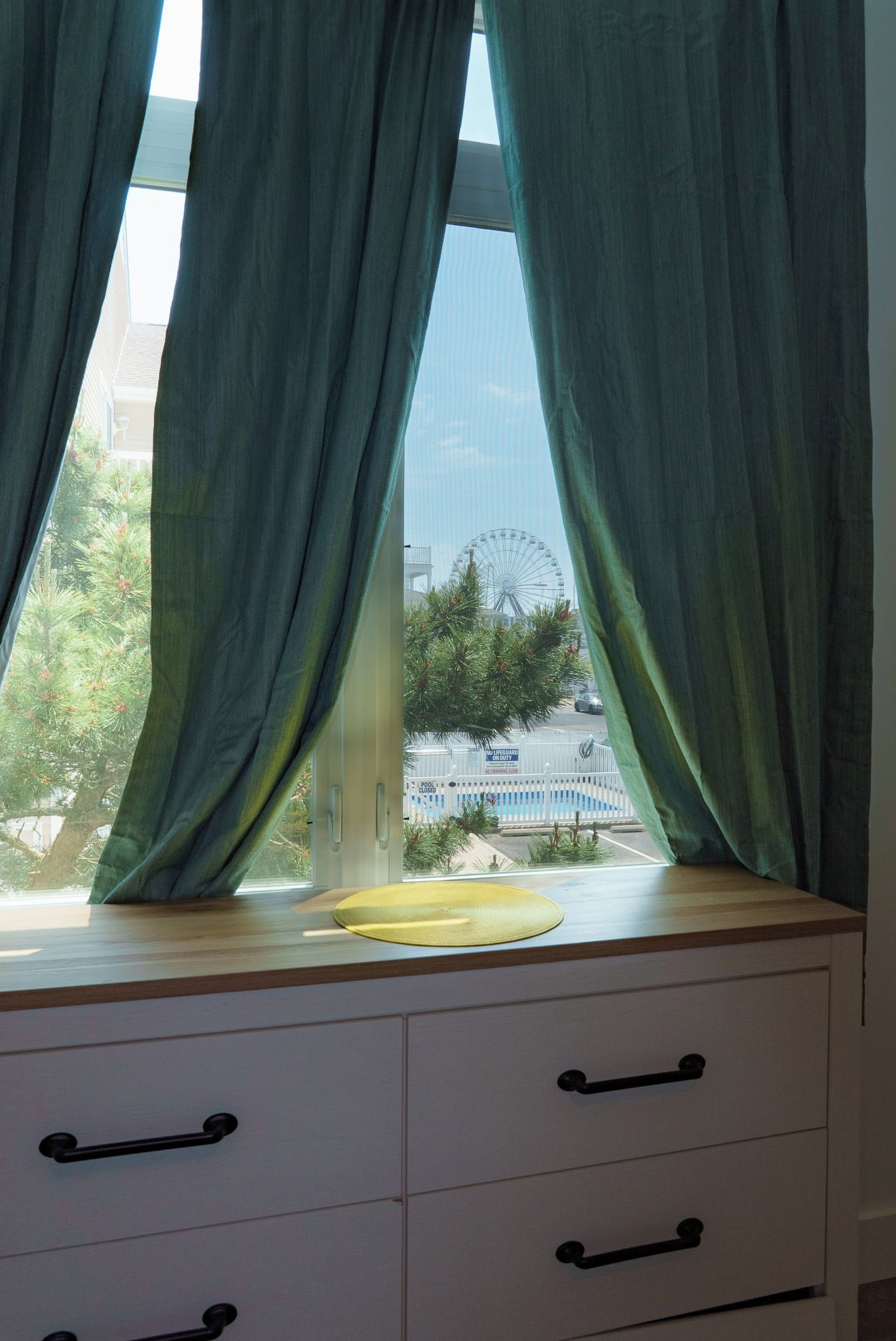 Une fenêtre avec des rideaux verts, un rebord de fenêtre en bois et un tapis jaune.