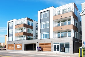 A multi-story residential building with a garage, a sign for 'Coral Sands Condominium,' and a parking sign. - Coastal Elegance - 1 Block to Beach - EV Charging - Parking (Seaside Heights)