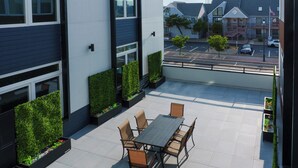Un patio moderno al aire libre con una mesa de comedor y sillas, rodeado de macetas con follaje.