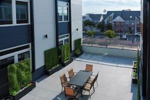 A modern outdoor patio with a dining table and chairs, surrounded by planters with greenery. - Coastal Elegance - 1 Block to Beach - EV Charging - Parking (Seaside Heights)