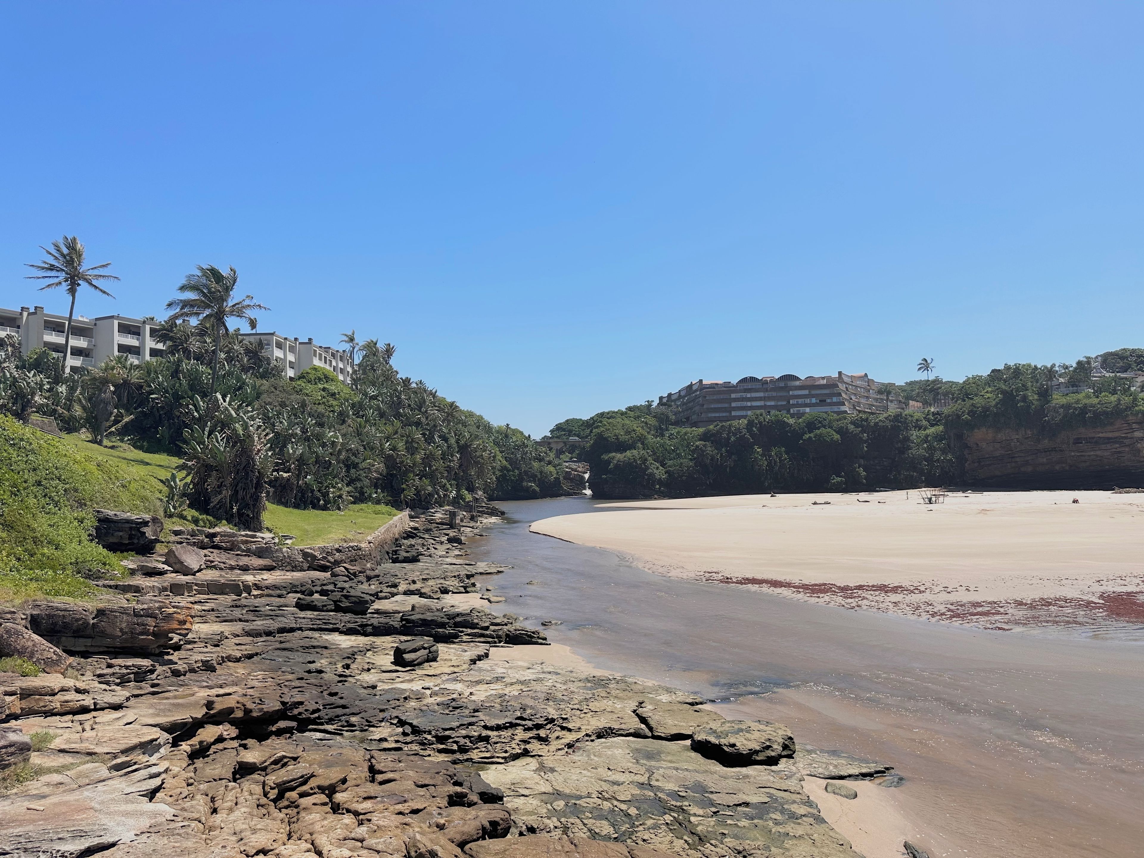 A coastal area with a rocky shoreline, a sandy beach, and buildings in the background.