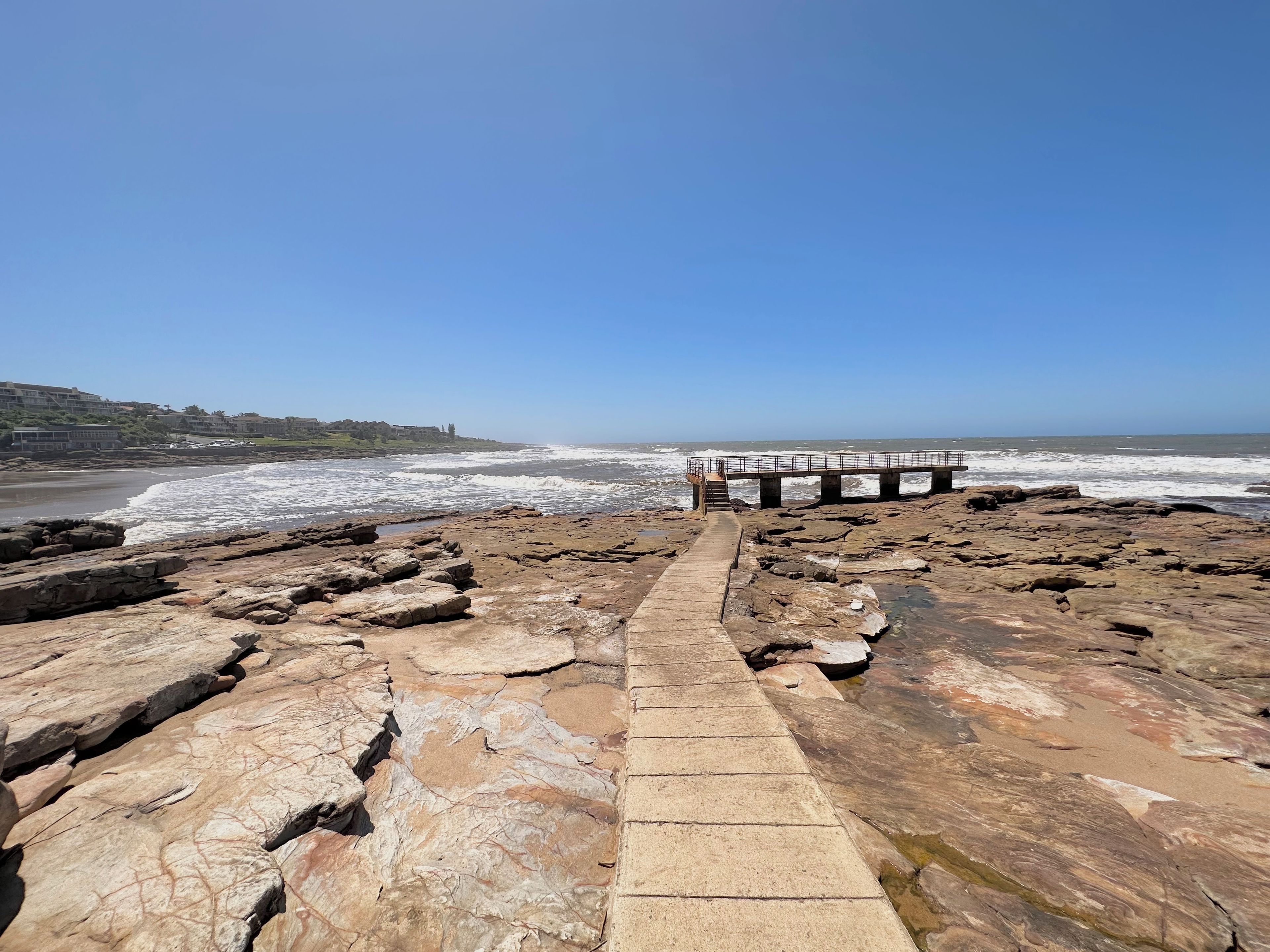 A rocky beach with a concrete walkway leading to a pier.