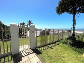 Una entrada protegida con reja a una zona de playa, con vista despejada al océano.