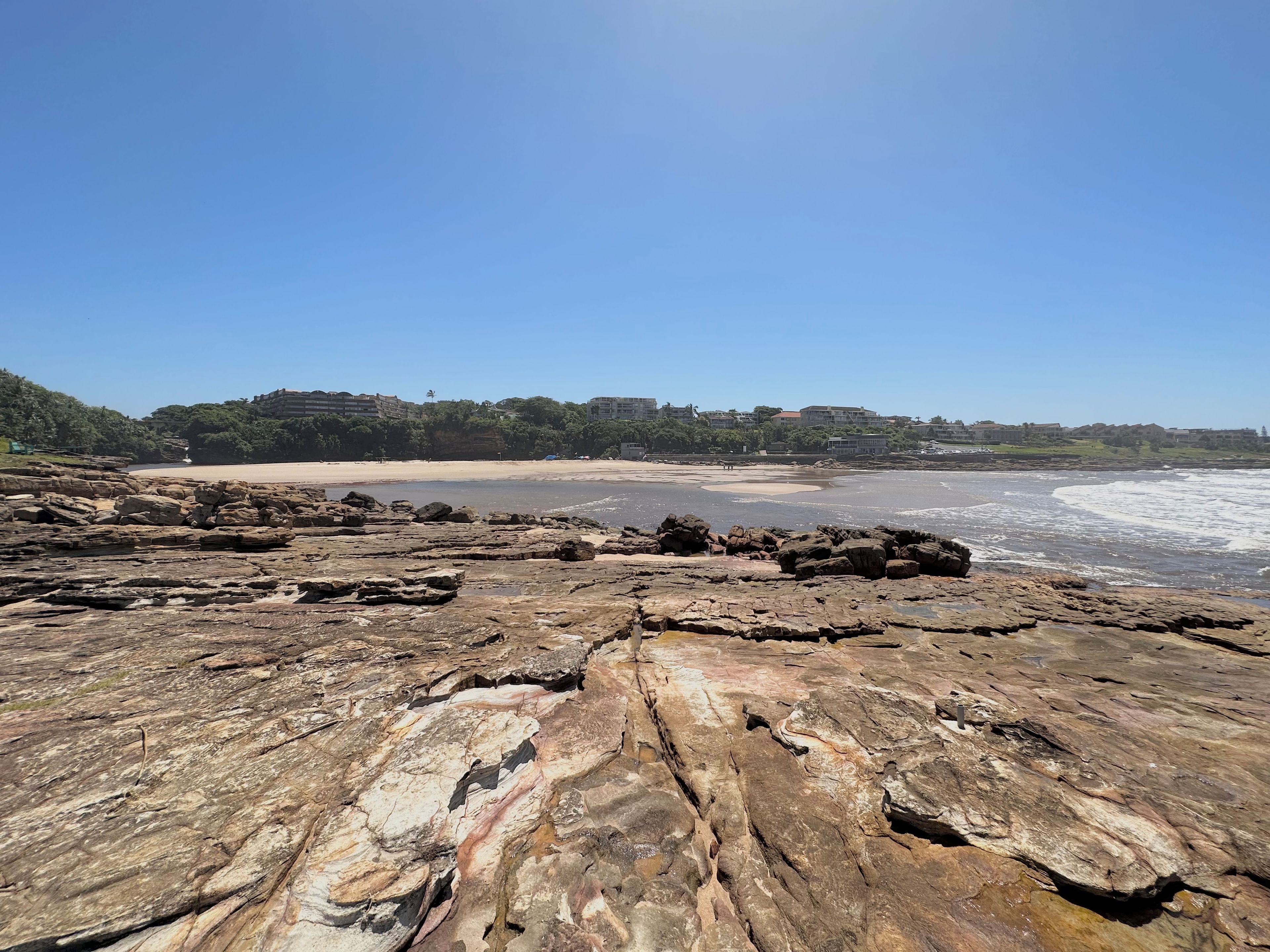 A rocky beach with a clear view of the ocean and distant buildings.