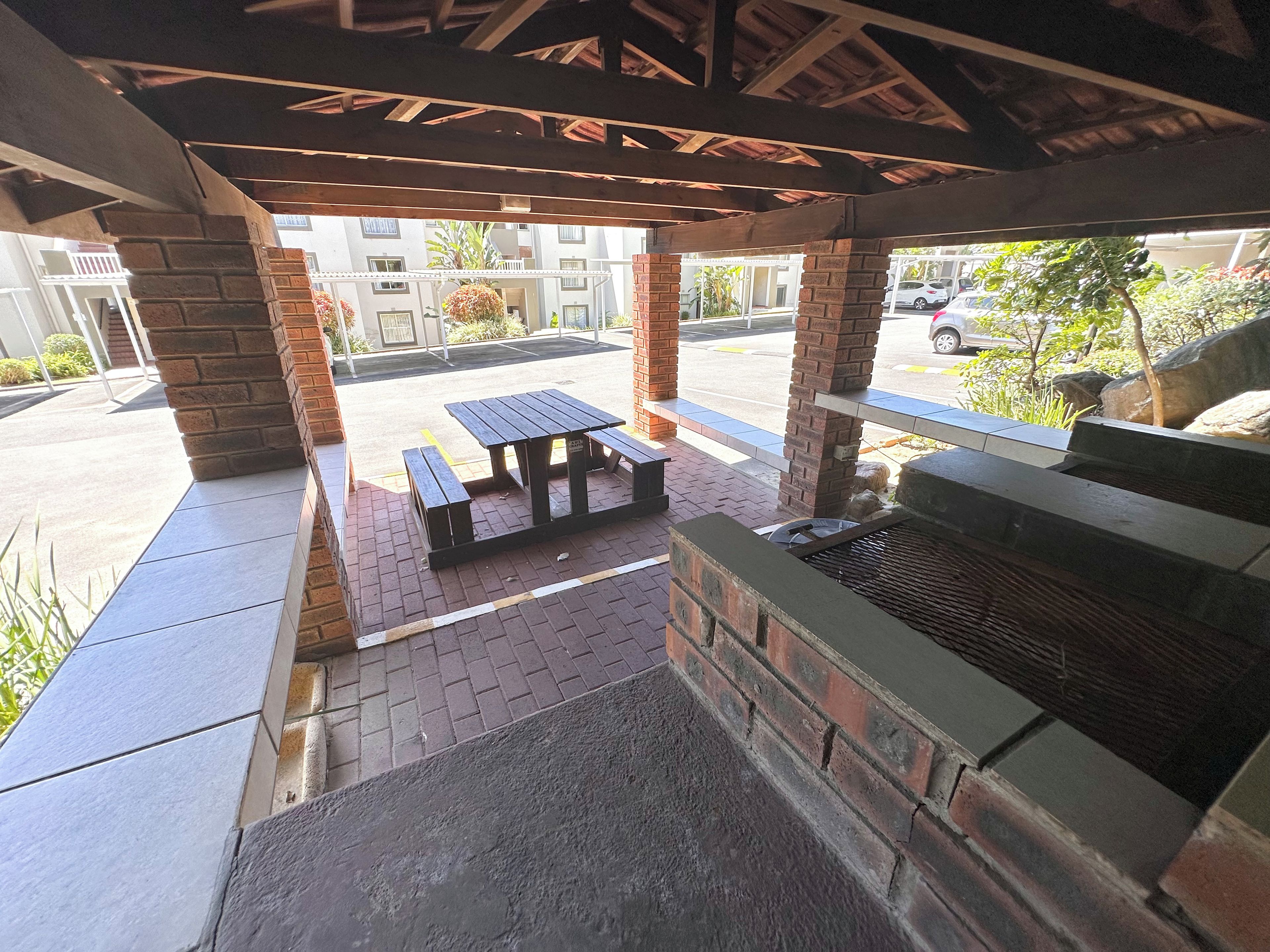 A covered outdoor seating area with a grill and picnic tables.